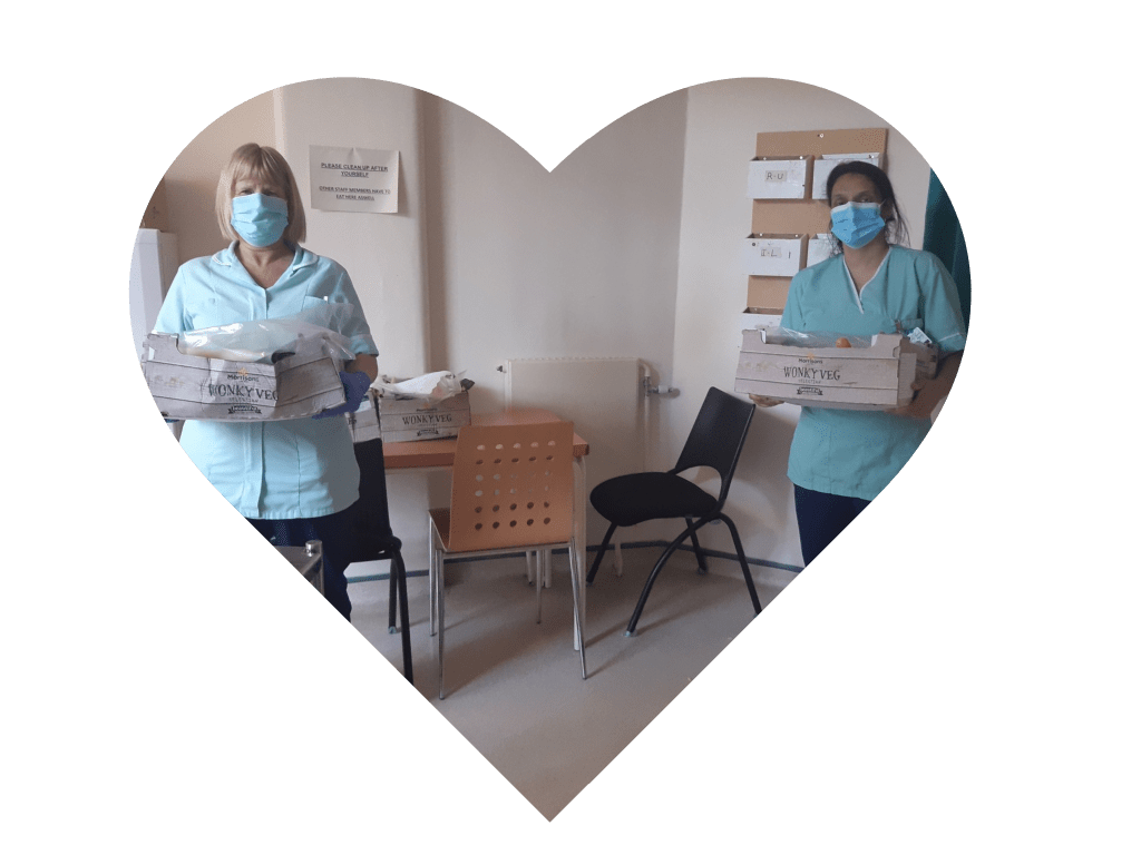 Two masked NHS workers standing apart, holding donated boxes of food